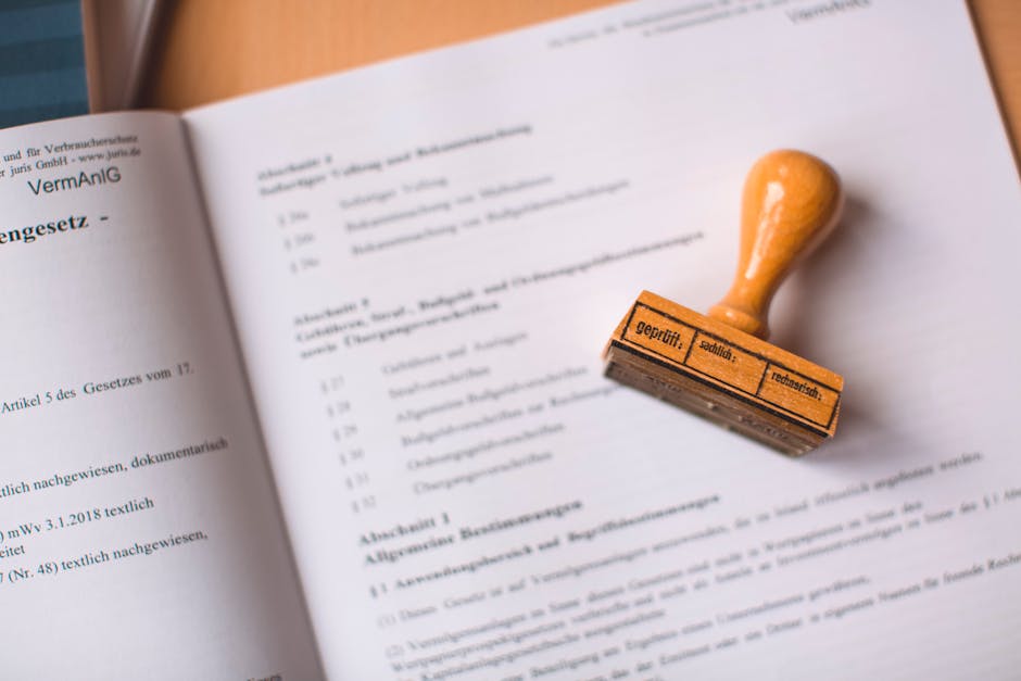 A close-up photograph of an open legal or official document with small, printed text on white paper. Resting on the page is a rubber stamp with an orange wooden handle and a rectangular orange rubber